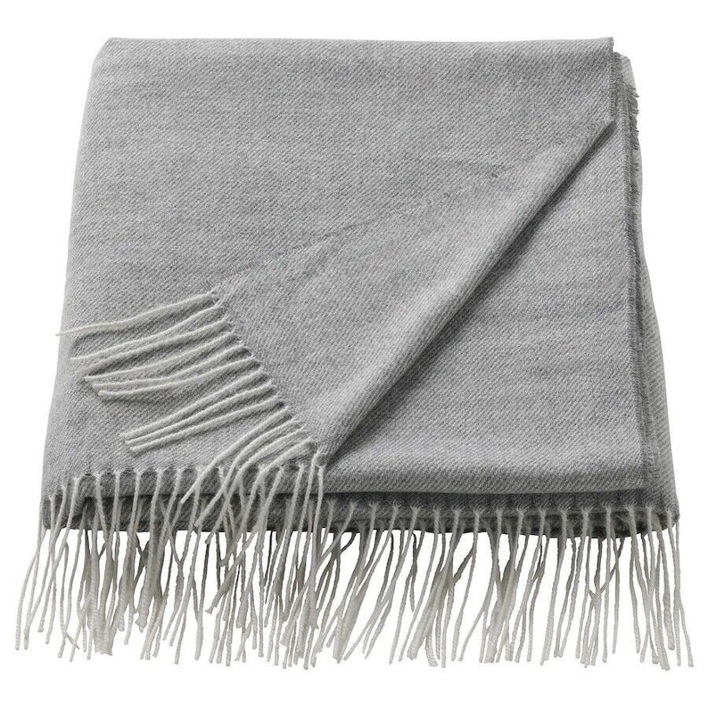 May include: A gray throw blanket with a white fringe. The blanket is folded in half and the fringe is visible on both sides.