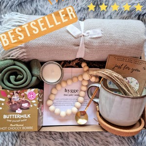 May include: A gift box filled with cozy items for self-care, including a soft blanket, a mug, a candle, a hot chocolate bomb, a wooden bead garland, and a card that says "just for you".