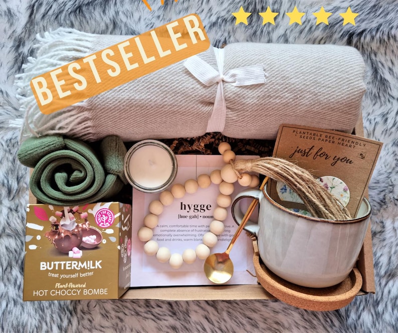 May include: A gift box filled with cozy items for self-care, including a soft blanket, a mug, a candle, a hot chocolate bomb, a wooden bead garland, and a card that says "just for you".