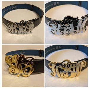 May include: Four different belt buckles with personalised monograms. The buckles are made of metal and have a shiny finish. The monograms are in a script font and are in different colours, including silver, gold, and black.
