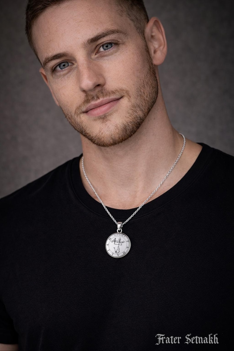 A man wearing a black t-shirt and a silver necklace with a pendant is shown in the image.