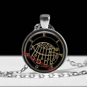 Op de afbeelding: Een zilverkleurige hanger aan een ketting met een ronde glazen cabochon. De inzet toont een zwarte achtergrond met een goudkleurig geometrisch zegel en de letters B, I, F, R, O, S eromheen. Rode tekst leest Sinah Ritual Art.