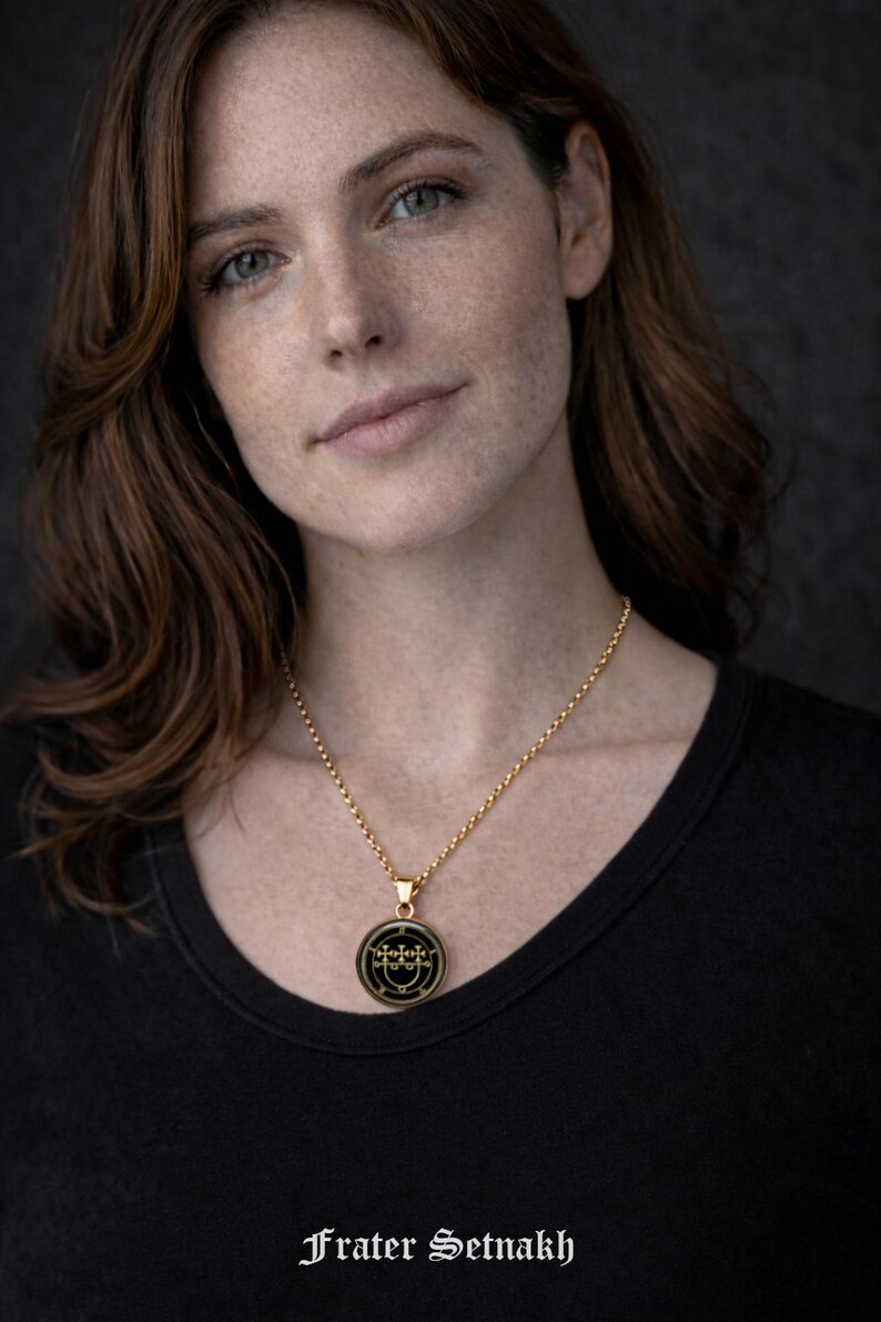 A portrait of a woman with long brown hair wearing a black top and a gold necklace with a pendant.