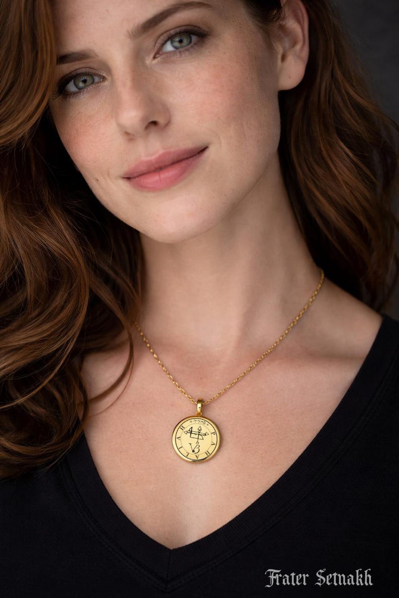 A close-up portrait of a woman with long brown hair, wearing a gold necklace with a round pendant. She is looking directly at the camera with a neutral expression.