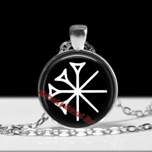May include: A silver-toned pendant necklace featuring a circular black charm with a white geometric design. The design resembles a stylized star or snowflake. The necklace has a delicate chain and a simple bail.