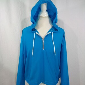 May include: A bright blue hooded sweatshirt with a white zipper and drawstring. The sweatshirt has long sleeves and a cropped hem.
