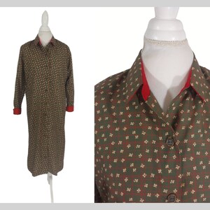 May include: A long-sleeved shirt dress with a green and white floral pattern. The shirt has a red collar and cuffs.