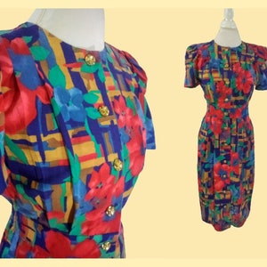 May include: A vintage dress with a vibrant floral pattern in red, blue, green, and yellow. The dress features short sleeves, a button-down front, and gold-colored buttons. The dress is displayed on a mannequin.