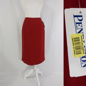 May include: A red knee-length skirt with a straight silhouette. The skirt has a waistband and a tag that reads "Pentagon, Proof of Purchase Required for Return".