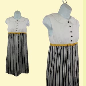 May include: A white sleeveless dress with a Peter Pan collar and black and white striped skirt. The dress has a yellow belt with a bow.