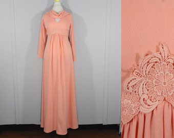 May include: A long peach-coloured maxi dress with a cowl neck and long sleeves. The dress has a lace trim around the neckline and a gathered waist.