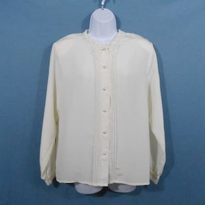 May include: A white long-sleeved blouse with a lace collar and pearl buttons.