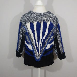 Puede incluir: Un suéter de punto con estampado geométrico en negro, blanco y azul. El suéter está hecho de un material suave y peludo.