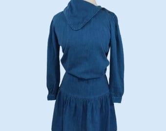 Puede incluir: Un vestido de mezclilla azul con mangas largas y un diseño de cuello único. El vestido presenta un corpiño ajustado y una falda acampanada con un dobladillo con volantes. El vestido se exhibe en un maniquí.