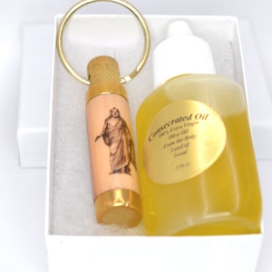Peut inclure: Un coffret cadeau contenant une petite bouteille d'huile d'olive et un flacon en bois avec un anneau doré. Le flacon porte une image d'une figure religieuse. La bouteille d'huile porte l'inscription "Huile Consacrée". L'ensemble est présenté dans une boîte blanche.