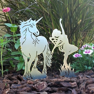 May include: Metal silhouette of a unicorn and a fairy standing in a garden setting. The unicorn is facing left and the fairy is facing right. Both are made of a silver-colored metal.