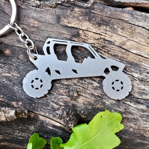 May include: A silver metal keychain shaped like a side-by-side off-road vehicle. The keychain is attached to a silver metal key ring.