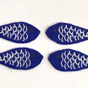May include: Four blue felt fish with silver embroidered scales. The fish are approximately 3 inches long.