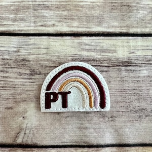 Peut inclure: Un patch en feutre blanc avec un arc-en-ciel brodé dans des tons de bordeaux, rose, beige et orange. Les lettres "PT" sont brodées en bordeaux au centre du patch.