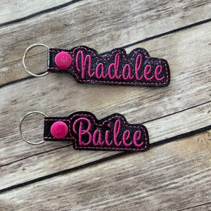 May include: Two black keychains with pink lettering. The top keychain says "Madalee" and the bottom keychain says "Bailee".