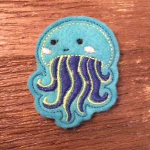 May include: A blue and green embroidered patch of a cartoon jellyfish with a smiling face and tentacles.