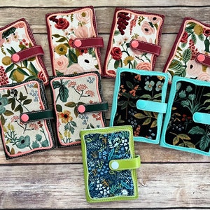 以下が含まれることがあります： 花柄の生地で覆われた財布が9つあります。財布はボタンとストラップが付いたフラップで閉じられます。財布は赤、緑、黒、青など、さまざまな色があります。