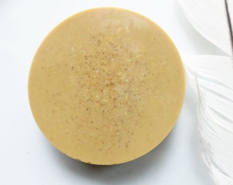 May include: A round, light brown soap bar with a speckled texture.