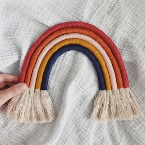Puede incluir: Adorno de pared hecho a mano con forma de arcoíris. El arcoíris está hecho con hilos de colores vibrantes: rojo, naranja, amarillo, rosa y azul. Tiene una franja en la parte inferior. Un elemento decorativo para la habitación de los niños.