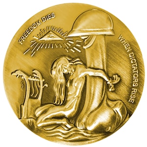 May include: A gold-colored coin with a raised image of a woman kneeling and holding onto a tree trunk. The text "FREEDOM DIES WHEN DICTATORS RISE" is inscribed around the edge of the coin. The coin also features a raised image of an eye inside a triangle.