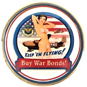 May include: A round, gold-rimmed pin with a white background. The pin features a woman in a red, white, and blue bikini, standing in front of a red, white, and blue American flag. The woman is holding her arms above her head. There are two airplanes in the background. The text "Keep 'em Flying! Buy War Bonds!" is written in red and white on a blue banner.