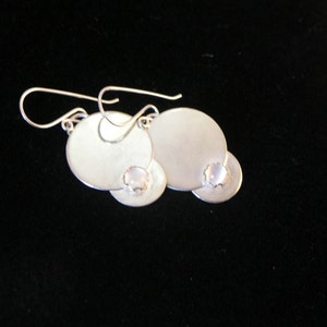 May include: Silver earrings with a round, white stone accent. The earrings are made of two overlapping circles.