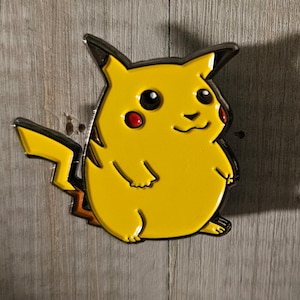 May include: A yellow enamel pin of Pikachu, a popular character from the Pokemon franchise. The pin is outlined in black and has red cheeks.