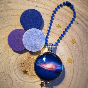 Peut inclure: Un collier avec un pendentif en argent en forme de médaillon contenant une image de galaxie bleue et rose. Le médaillon est sur une chaîne bleue et est entouré de petites étoiles dorées.