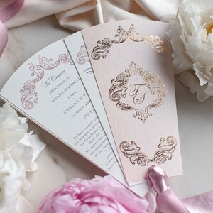 May include: A pink and white wedding ceremony programme fan with gold foil accents. The text on the fan reads "The Ceremony" and includes the order of events.