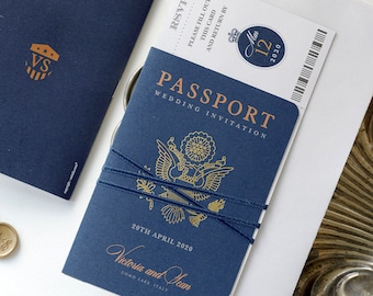 May include: A navy blue passport-style wedding invitation with gold foil accents. The front of the invitation features a gold eagle design and the text "PASSPORT WEDDING INVITATION". The date "20TH APRIL 2020" and the names "Victoria and Yean" are printed in gold foil. The invitation is tied with a navy blue ribbon.