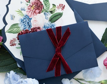 Puede incluir: Un sobre azul marino con una cinta de terciopelo burdeos atada en un lazo. El sobre está decorado con un diseño floral con flores rosas, rojas y azules. El texto "RESPONSE" es visible en la parte superior del sobre.