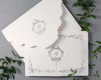 Puede incluir: Una invitación de boda blanca con un diseño de lámina plateada. La invitación presenta un borde decorativo y un monograma en el centro.