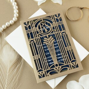 May include: Gold laser cut wedding invitation with a navy blue inner layer. The invitation features a monogram of the letters "R" and "S" in a decorative frame. The text on the invitation reads "Request the pleasure of your company for dinner" and includes the date, time, and location of the wedding.