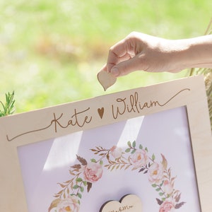 Puede incluir: Un marco de madera con un dise&ntilde;o floral y el texto "Kate &hearts; William" en la parte superior. Se coloca un coraz&oacute;n de madera en el marco.