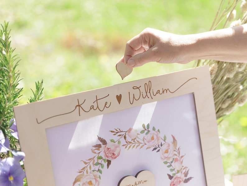 Puede incluir: Un marco de madera con un dise&ntilde;o floral y el texto "Kate &hearts; William" en la parte superior. Se coloca un coraz&oacute;n de madera en el marco.