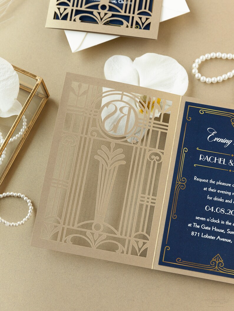 May include: A gold and blue wedding invitation with a laser cut design. The invitation features the text "Evening" and "Rachel &" in gold lettering on a navy blue background. The date "04.08.20" is also included.