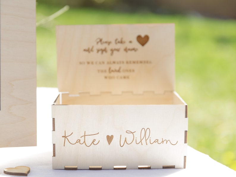 Puede incluir: Una caja de madera con una ranura en la parte superior para tarjetas. La caja est&aacute; grabada con el texto "T&oacute;mate siempre un momento para apreciar las cosas buenas de la vida" y "Para que siempre podamos recordar los buenos momentos que pasamos." La caja tambi&eacute;n est&aacute; grabada con los nombres "Kate" y "William" y un s&iacute;mbolo de coraz&oacute;n.