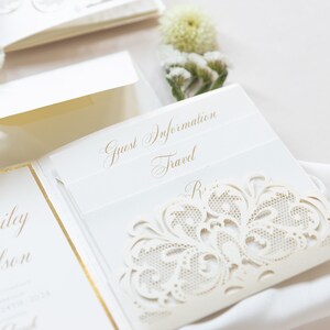 May include: A white wedding invitation with a gold border and a delicate lace design. The invitation includes the text "Guest Information" and "Travel".