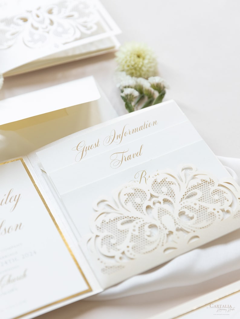 May include: A white wedding invitation with a gold border and a delicate lace design. The invitation includes the text "Guest Information" and "Travel".