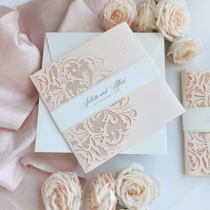 May include: A blush pink wedding invitation with a delicate laser-cut floral design. The invitation reads "Juliette and Albert, September 24th, 2021".