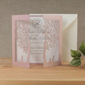May include: Pink laser cut wedding invitation with a tree design. The invitation reads "Rachel and Jonathan" with the date "23rd February".