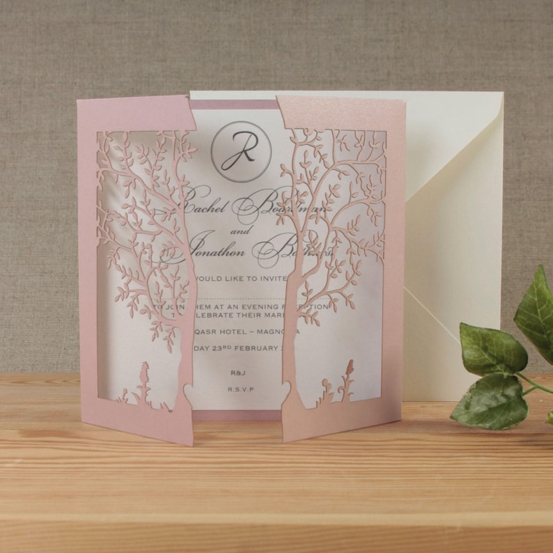May include: Pink laser cut wedding invitation with a tree design. The invitation reads "Rachel and Jonathan" with the date "23rd February".