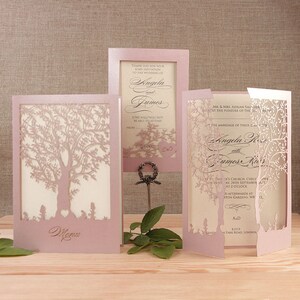 May include: Pink wedding invitation with a laser cut tree design. The invitation includes the names "Angela" and "James" and the date "September 24th".