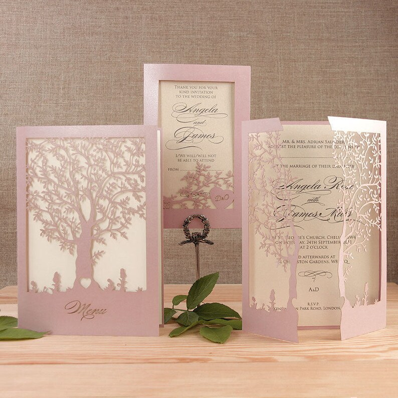 May include: Pink wedding invitation with a laser cut tree design. The invitation includes the names "Angela" and "James" and the date "September 24th".