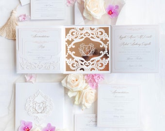 May include: White wedding invitation suite with gold accents. The invitation features a laser-cut design with a floral motif. The RSVP card and accommodation card are also included. The invitation is decorated with white and pink flowers.